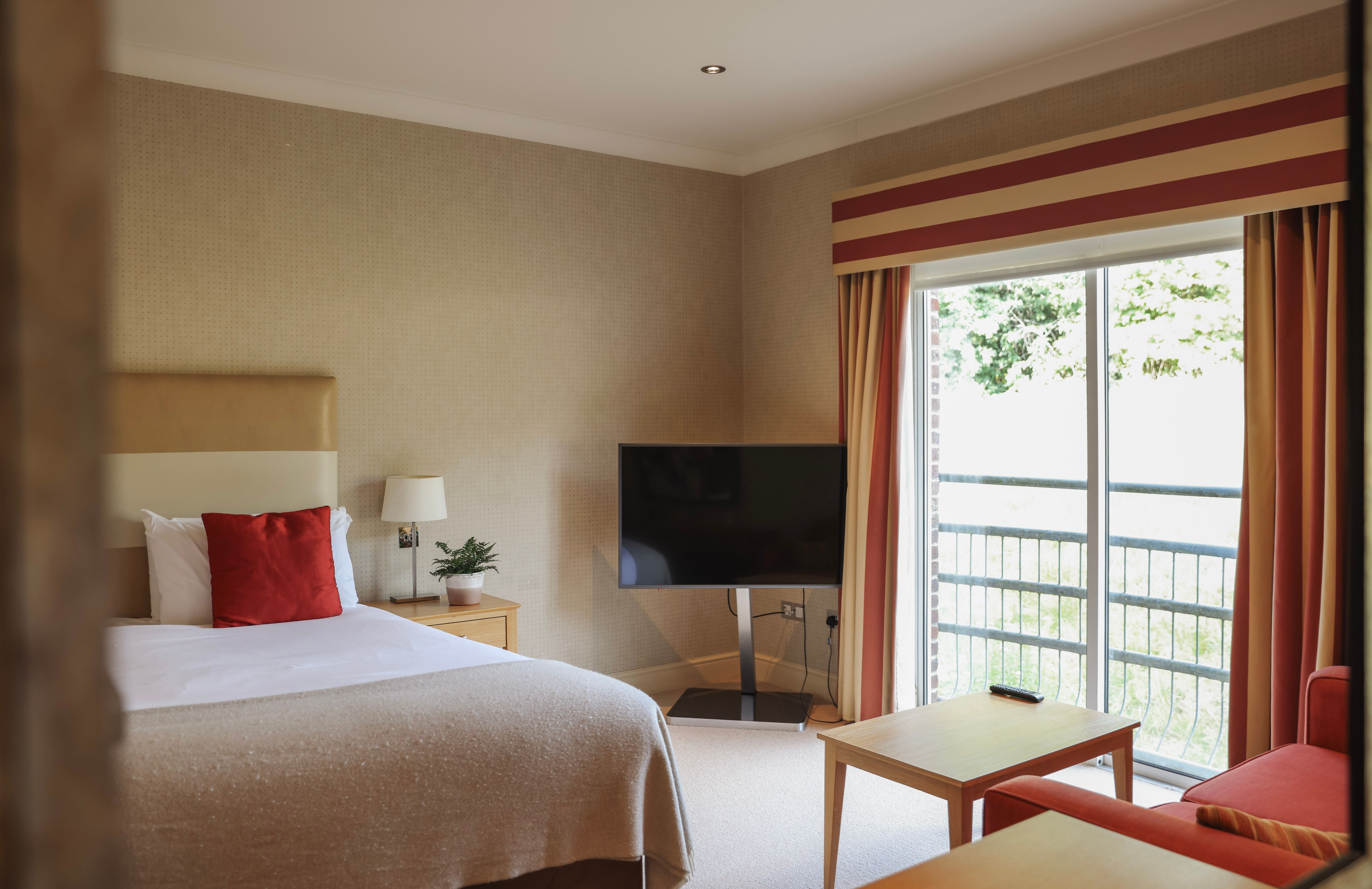 Modern hotel room with a bed, television, window with curtains, and a balcony view
