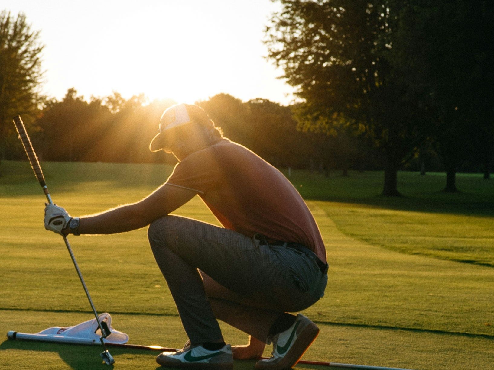 Golfer squatting on the green at sunset, preparing for a putt.