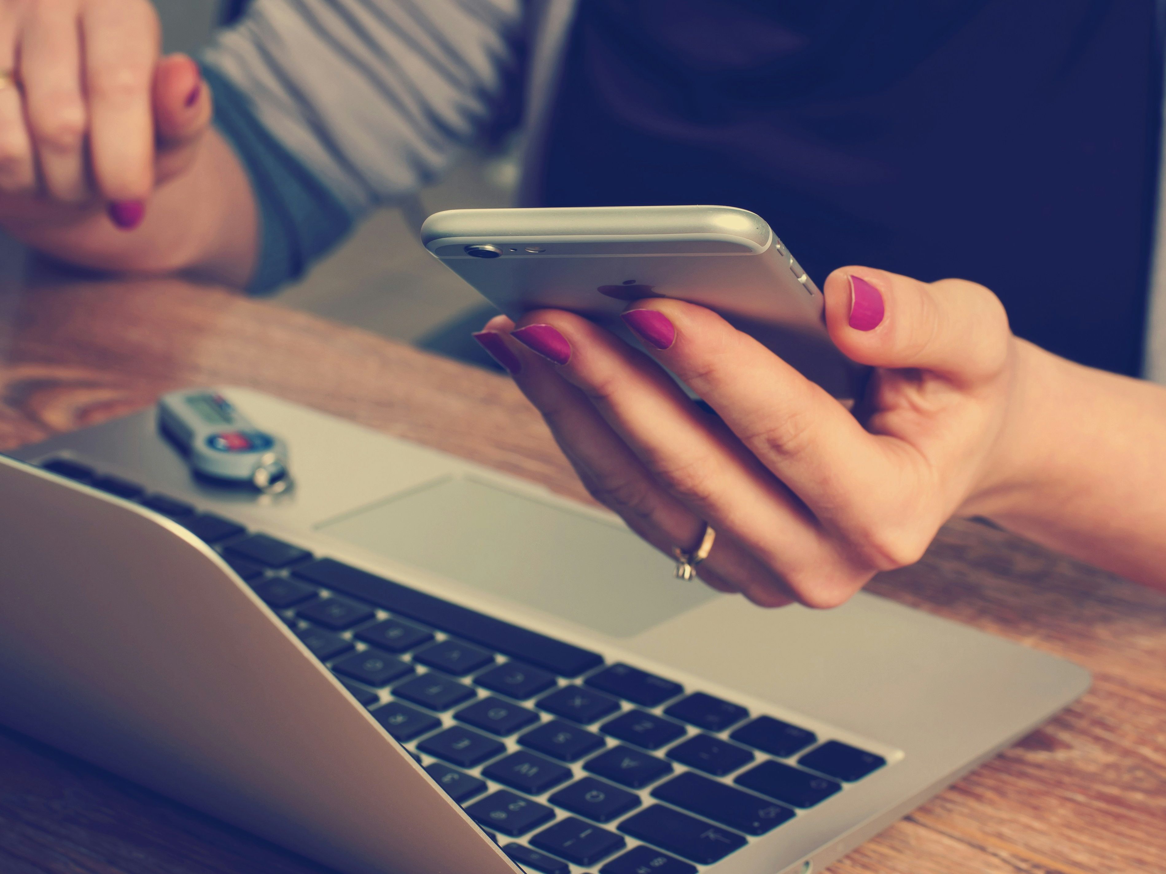 Person holding a smartphone near a laptop with a USB drive on the keyboard