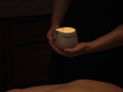 A person holds a white ceramic container with a lit candle inside during a massage session.
