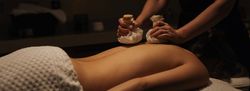A person receiving a relaxing herbal compress massage on their back at a spa.