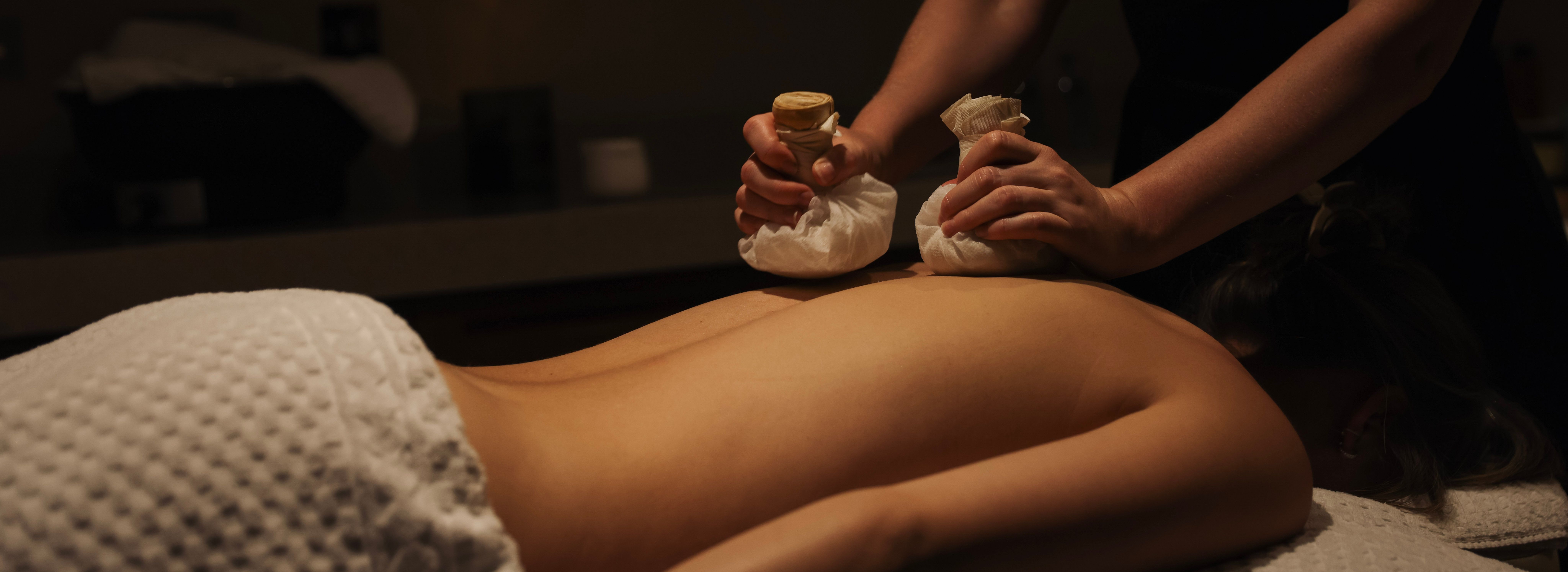A person receiving a relaxing herbal compress massage on their back at a spa.