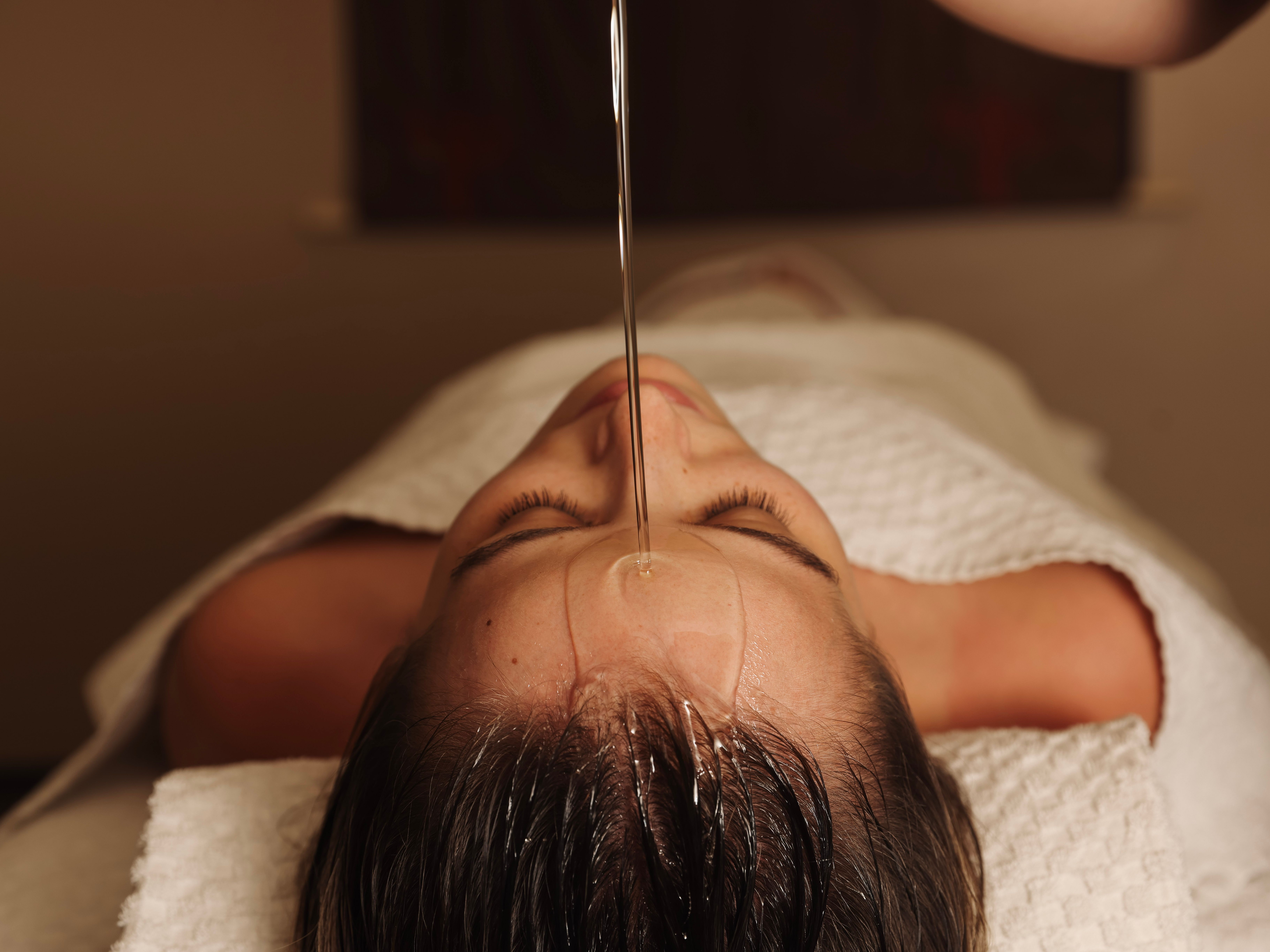 Person receiving oil therapy on forehead while lying down