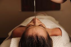 Person receiving oil therapy on forehead while lying down