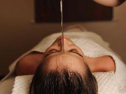 Person receiving oil therapy on forehead while lying down