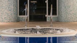Indoor hot tub with bubbling water next to a blue-tiled wall and glass door.