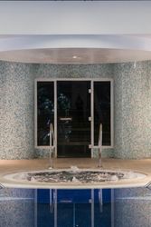 Indoor hot tub with bubbling water next to a blue-tiled wall and glass door.