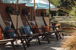Outdoor wooden lounge chairs with colorful pillows under blue umbrellas at a patio area.