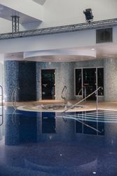 Indoor swimming pool area with a hot tub and blue mosaic tiles on the walls.
