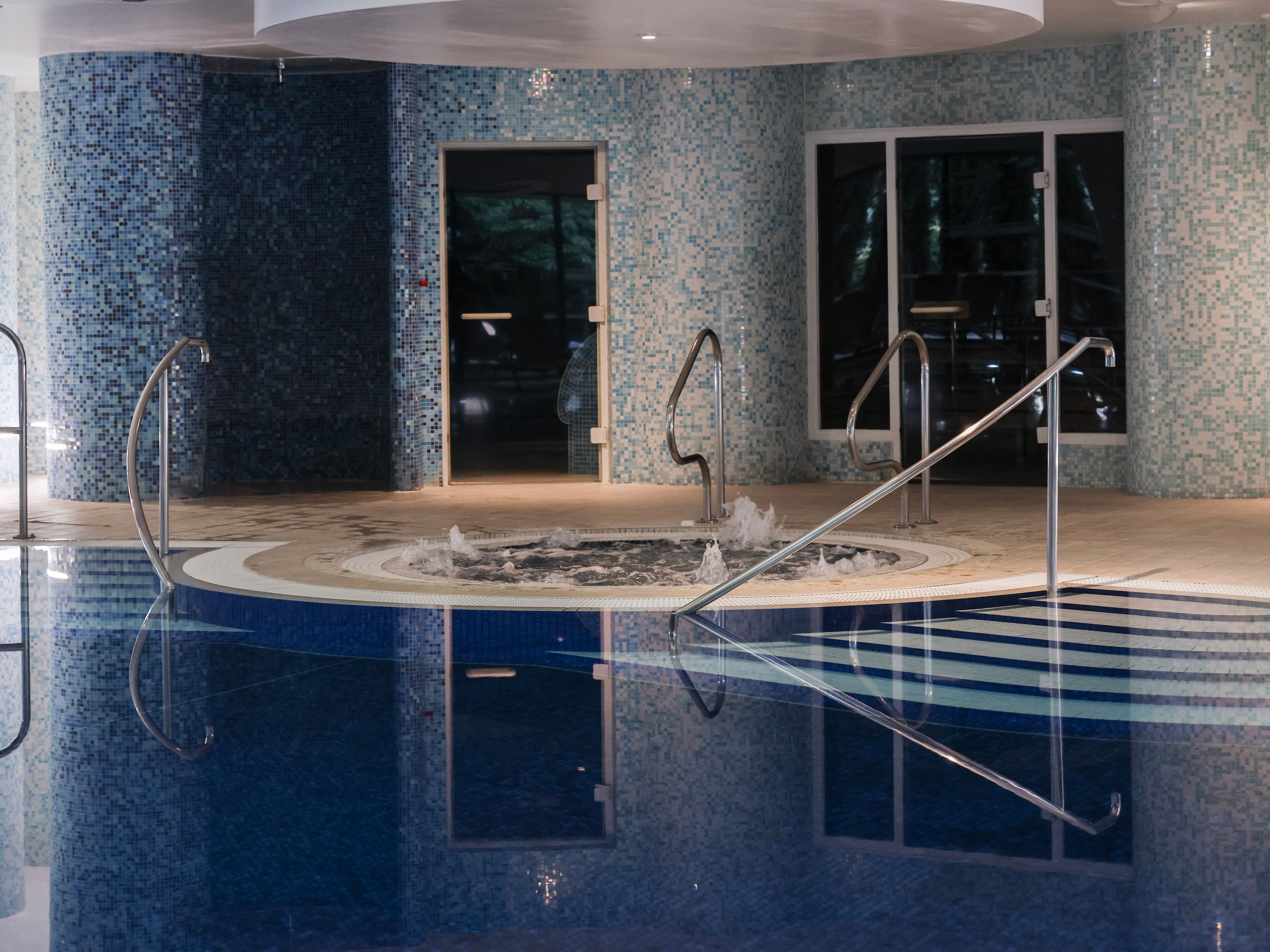 Indoor swimming pool area with a hot tub and blue mosaic tiles on the walls.