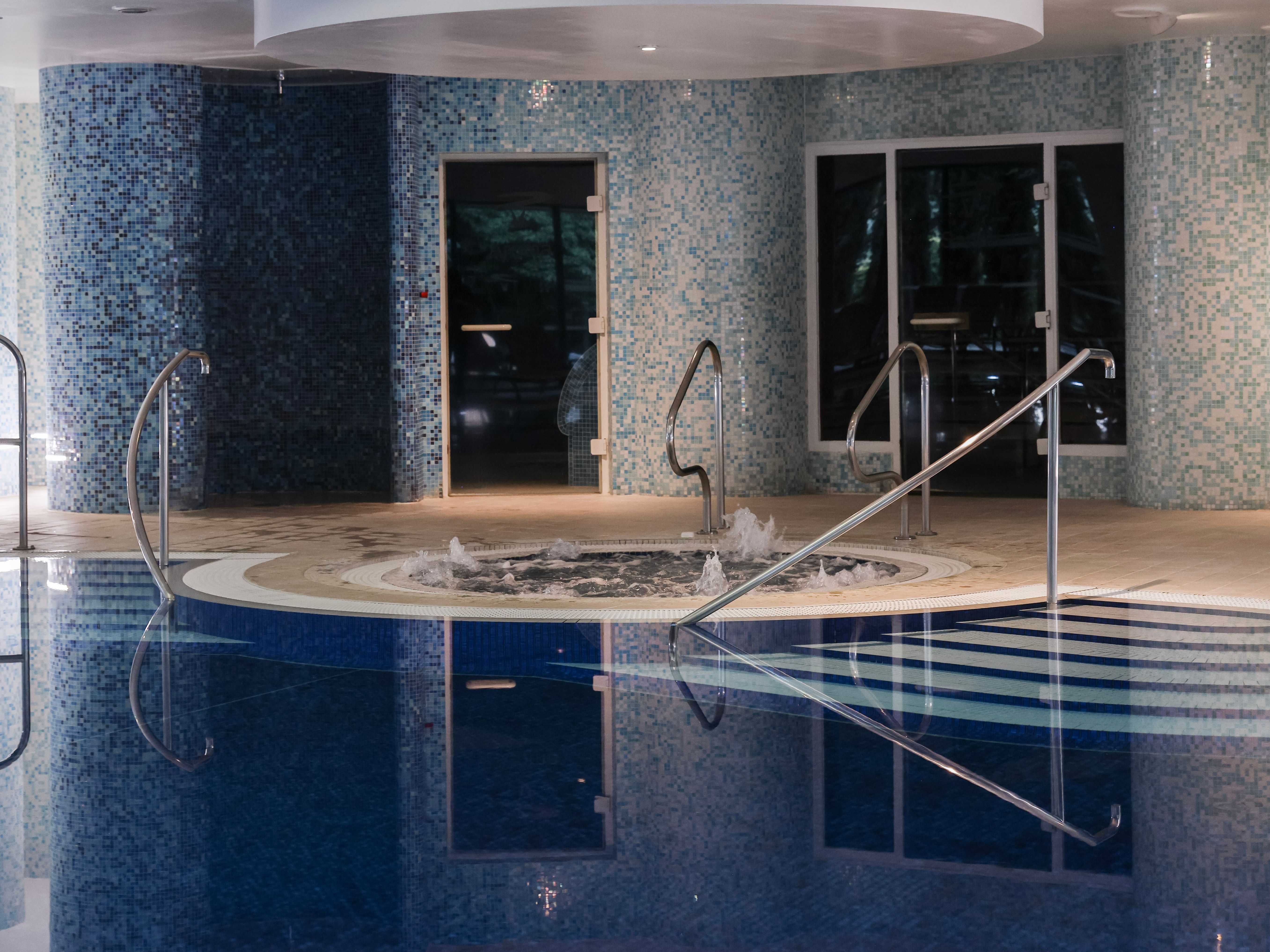 Indoor swimming pool area with a hot tub and blue mosaic tiles on the walls.