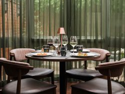 Elegant dining table set for four with wine glasses, plates of food, and a small lamp in a modern restaurant setting.