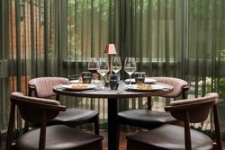 Elegant dining table set for four with wine glasses, plates of food, and a small lamp in a modern restaurant setting.
