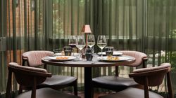 Elegant dining table set for four with wine glasses, plates of food, and a small lamp in a modern restaurant setting.