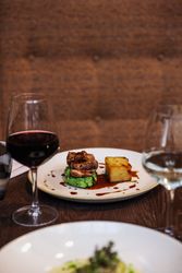 Gourmet plated meal with a glass of red wine and a glass of white wine on a dark restaurant table.