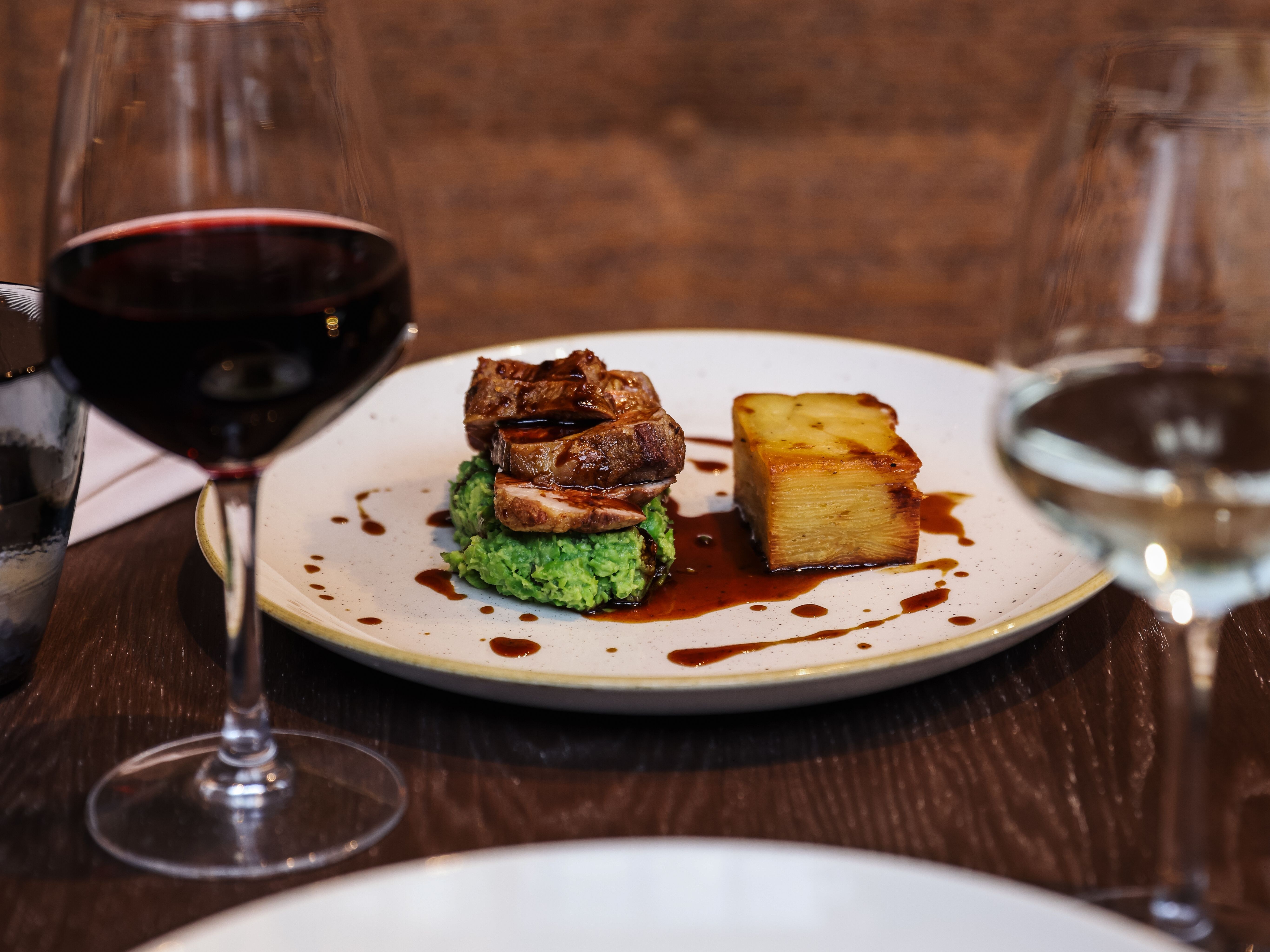 Gourmet plated meal with a glass of red wine and a glass of white wine on a dark restaurant table.