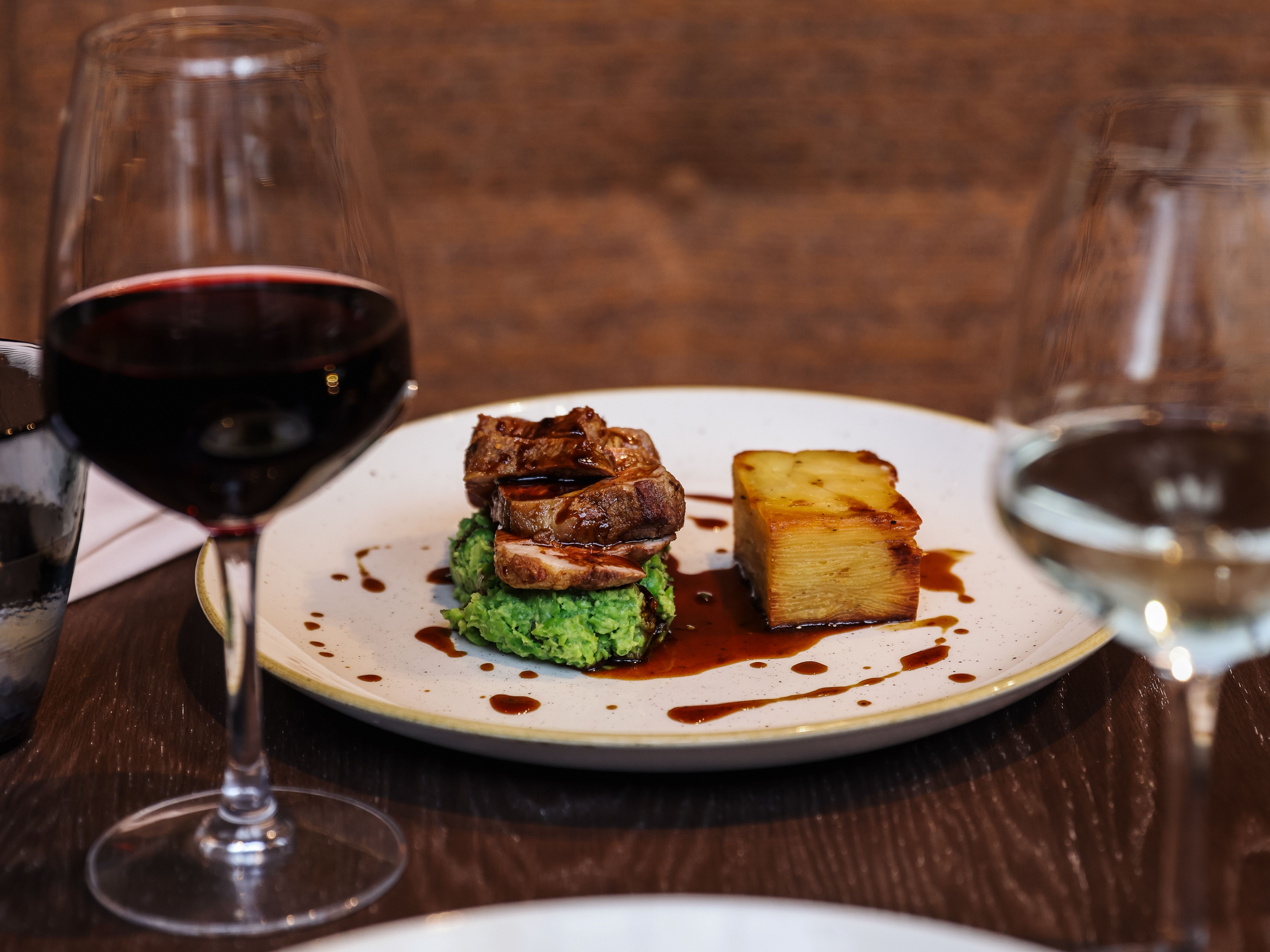 Gourmet plated meal with a glass of red wine and a glass of white wine on a dark restaurant table.