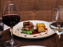 Gourmet plated meal with a glass of red wine and a glass of white wine on a dark restaurant table.
