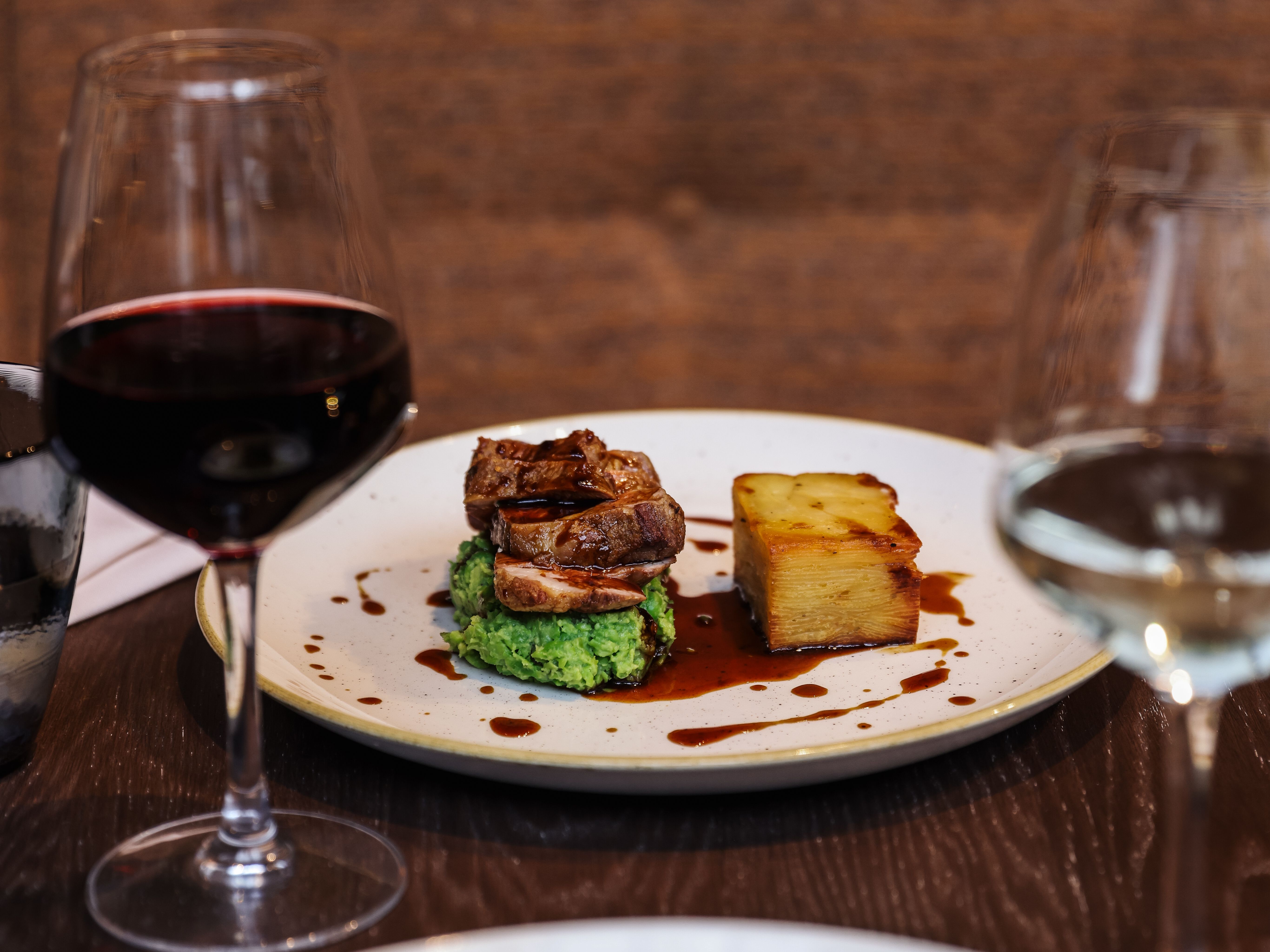 Gourmet plated meal with a glass of red wine and a glass of white wine on a dark restaurant table.