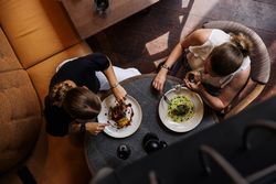 Two women dining at a restaurant table, viewed from above, enjoying plated gourmet meals and drinks.