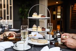 A tiered tray filled with assorted pastries and sandwiches, with tea cups, glasses of champagne, and people enjoying afternoon tea