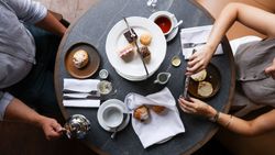 Table set for afternoon tea with pastries, scones, and tea, seen from above