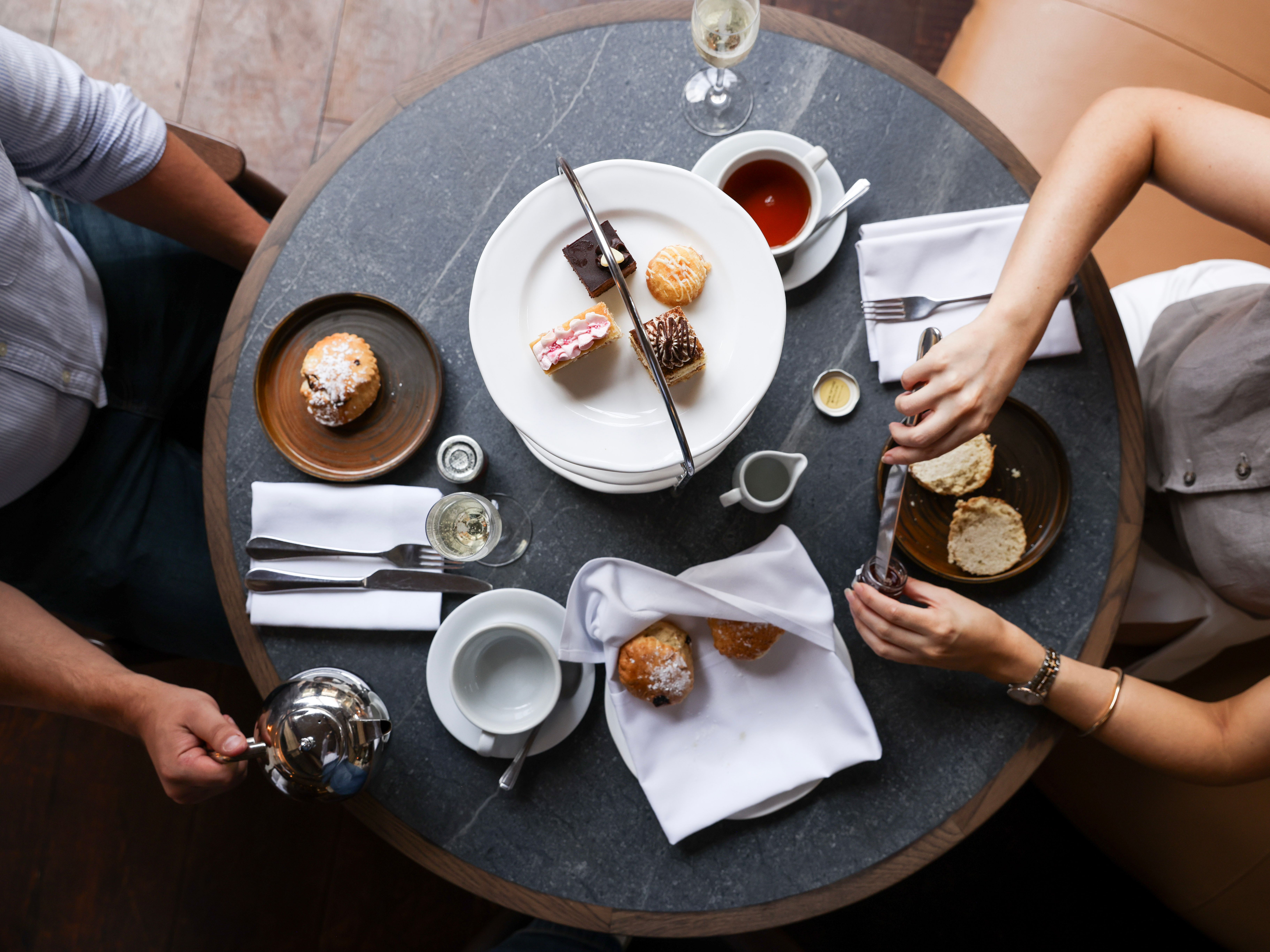 Table set for afternoon tea with pastries, scones, and tea, seen from above