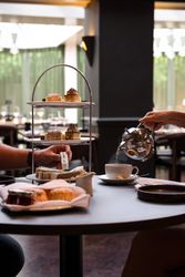 Afternoon tea with a tiered tray of cakes and sandwiches, a person pouring tea into a cup.