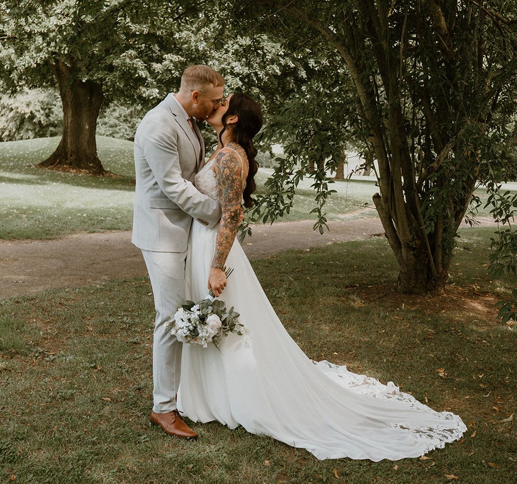Bride and groom kissing under a tree in a park setting.