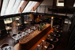 Modern restaurant interior with wooden tables, cushioned seating, and large windows