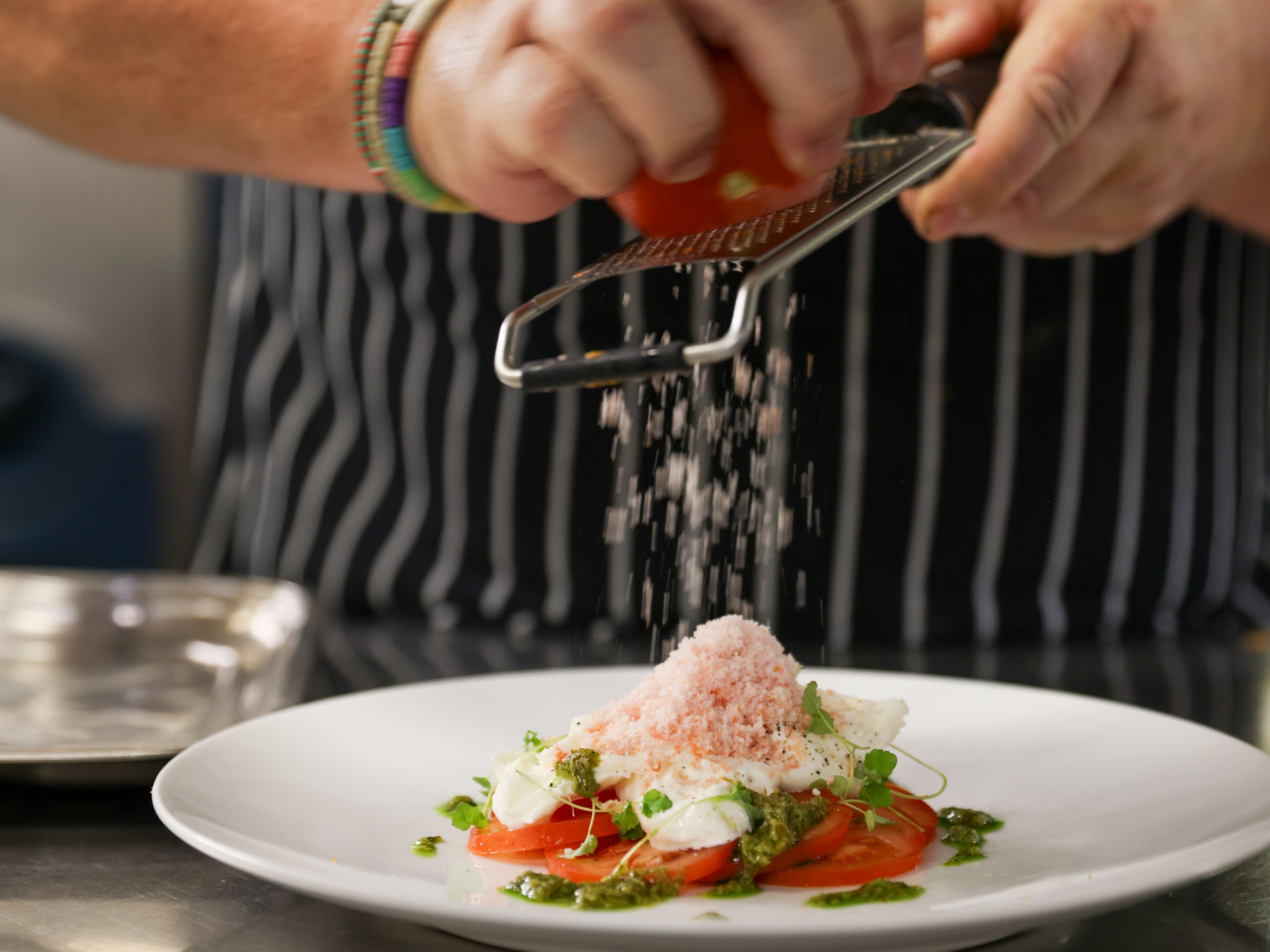 Chef grating an ingredient over a plated dish in a kitchen