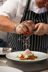 Chef grating an ingredient over a plated dish in a kitchen