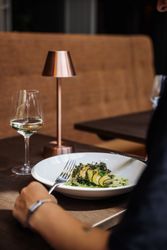 A person dining at a restaurant with a plate of elegantly plated food, a glass of white wine, and a small copper table lamp