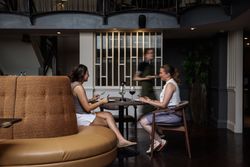 Two women sitting at a restaurant table with drinks, being served by a waiter.