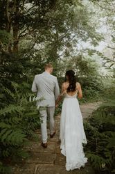 Bride and groom holding hands walking along a stone path surrounded by lush greenery.