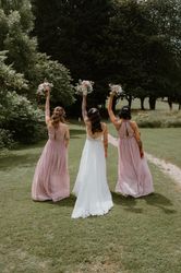 Bride and bridesmaids with bouquets held high walking away on a grassy path outdoors