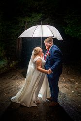 Bride and groom standing under an umbrella at night, holding hands and smiling at each other