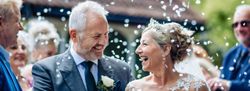 Smiling bride and groom during outdoor wedding ceremony with guests throwing confetti.