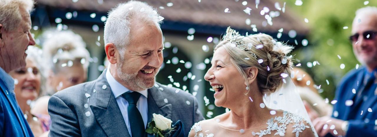 Smiling bride and groom during outdoor wedding ceremony with guests throwing confetti.