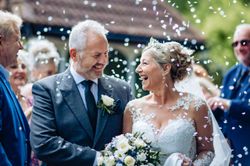 Smiling bride and groom during outdoor wedding ceremony with guests throwing confetti.