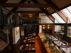 Modern restaurant interior with wooden beams, large windows, and cozy dining tables.