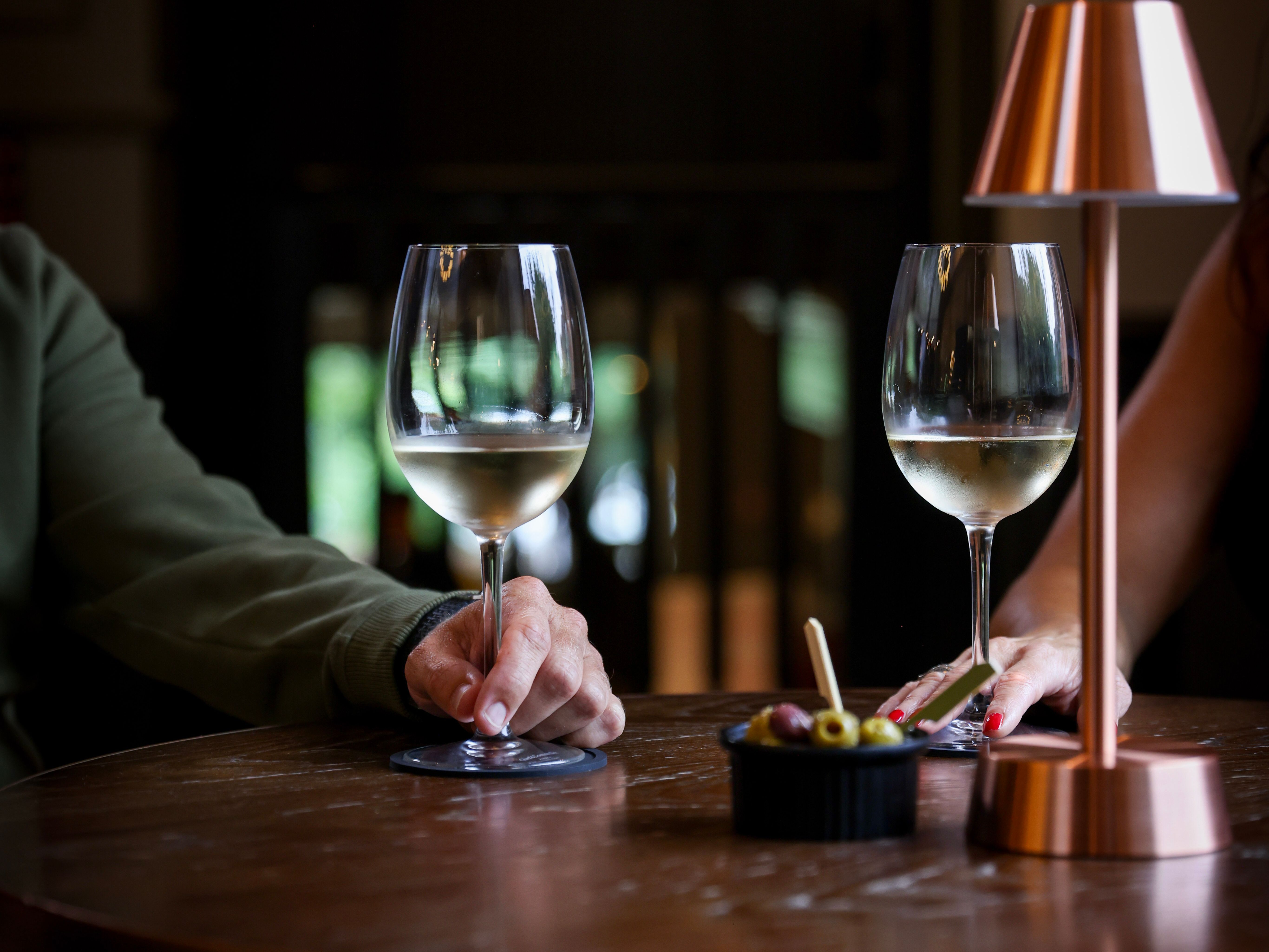 Two people sitting at a table with glasses of white wine, a small lamp, and a dish of olives.