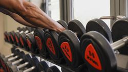 Person reaching for a dumbbell on a rack in a gym