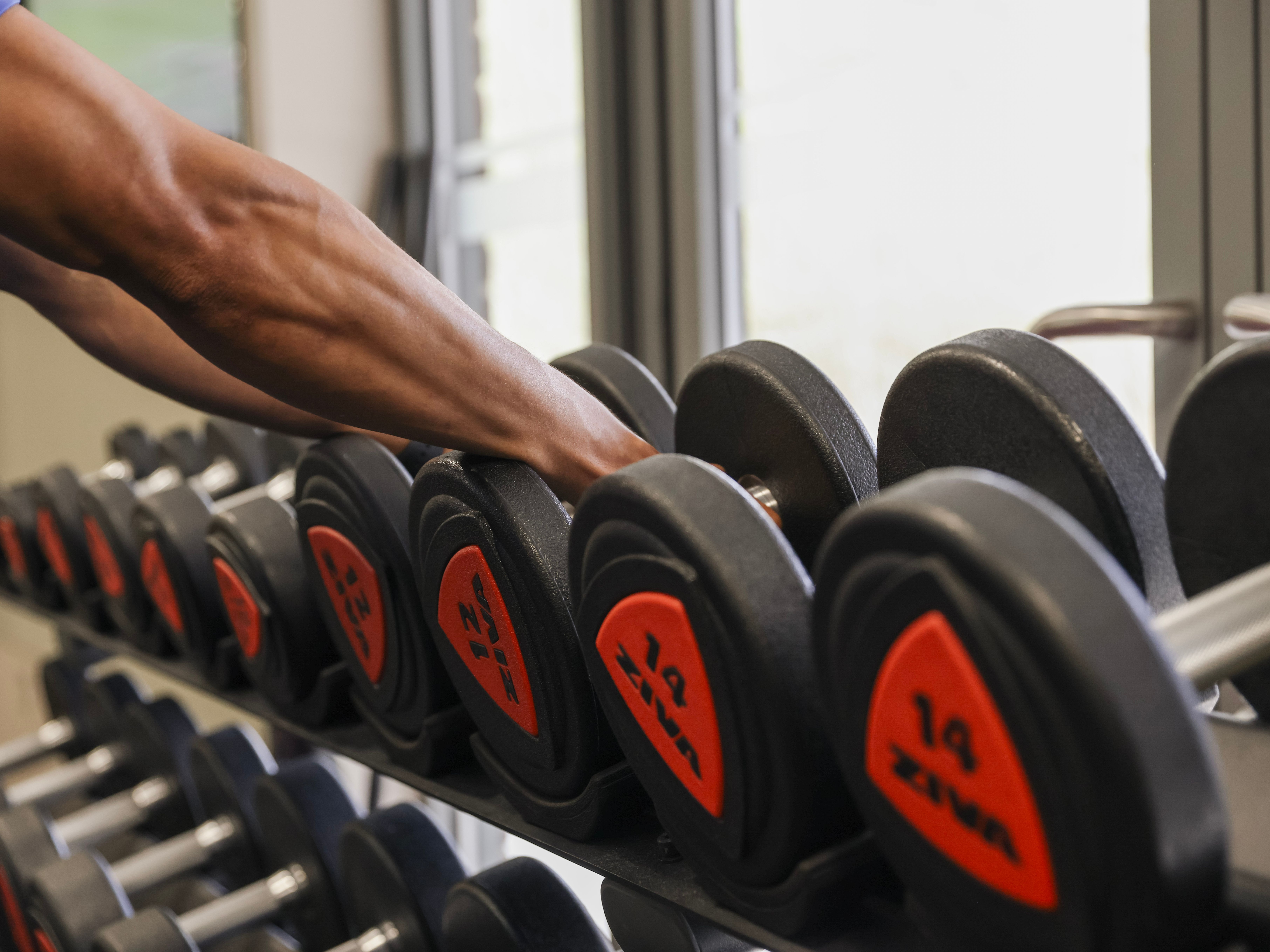 Person reaching for a dumbbell on a rack in a gym