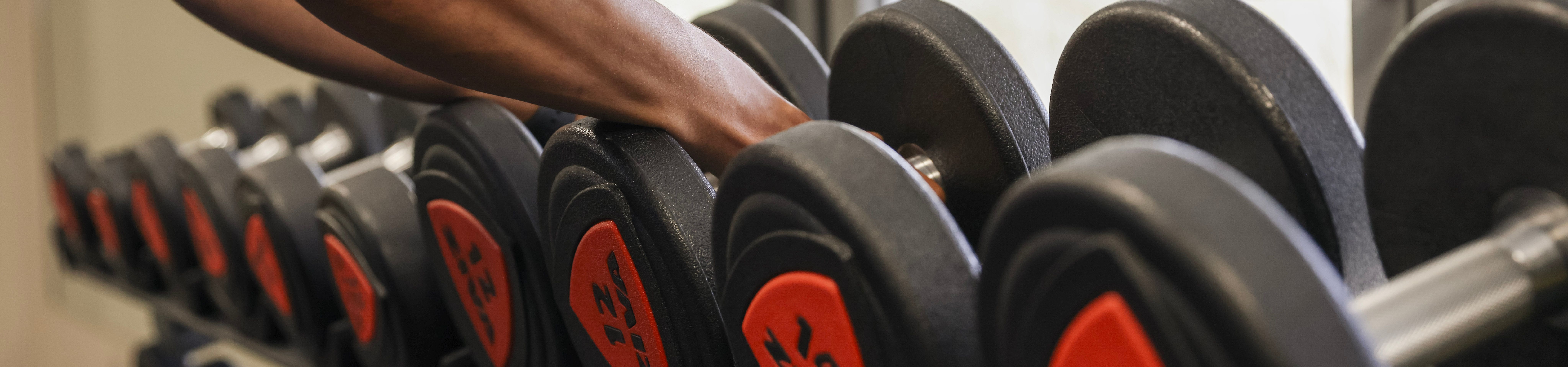 Person reaching for a dumbbell on a rack in a gym