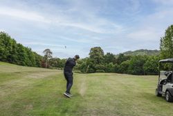 Golfer swinging a club on a lush, green golf course with a golf cart nearby