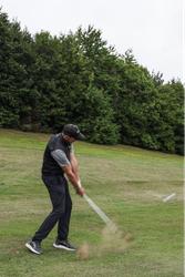 Golfer swinging a club on a grassy course with trees in the background.