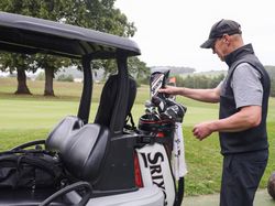 Man preparing golf clubs beside a golf cart on a golf course