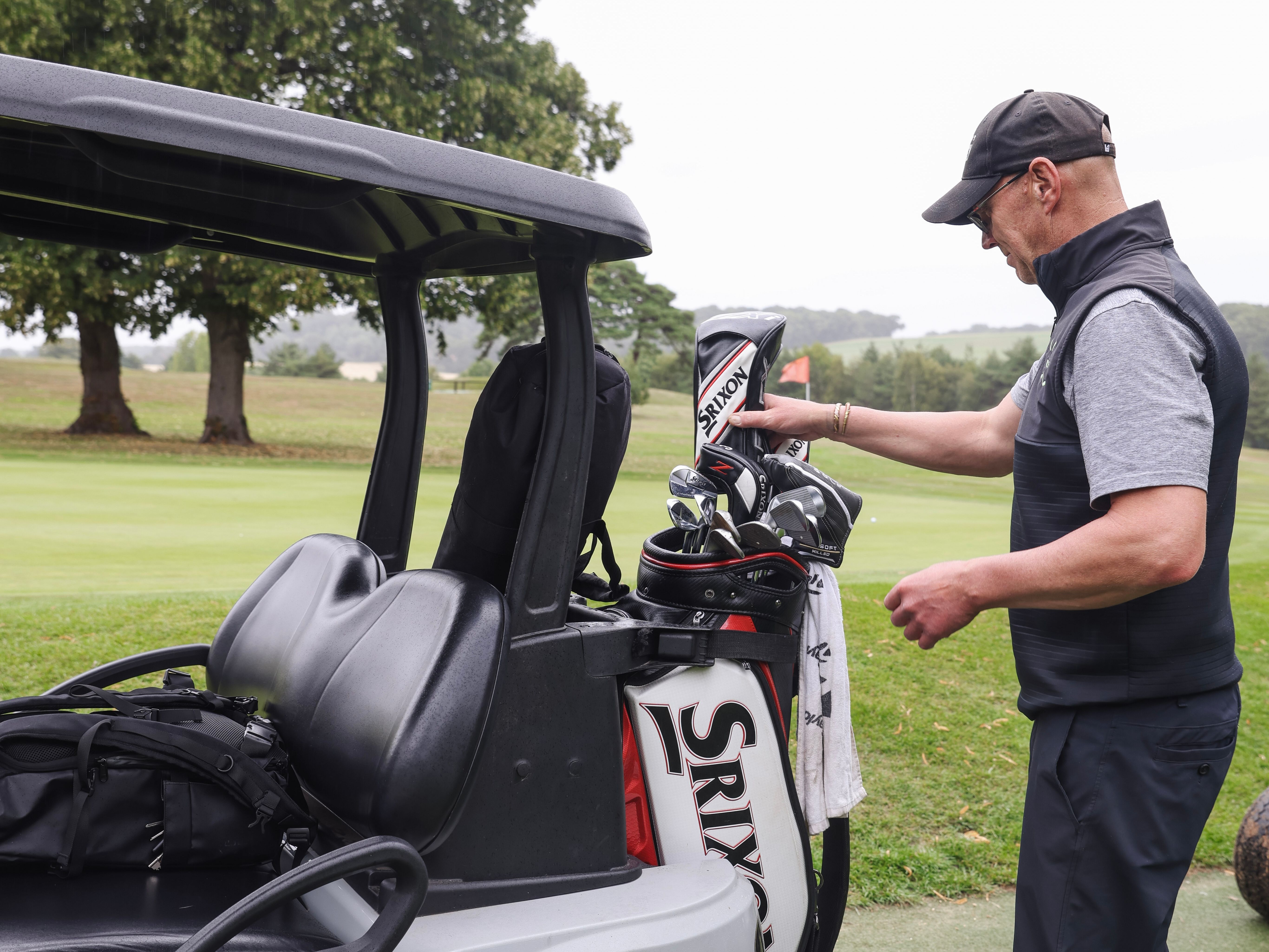 Man preparing golf clubs beside a golf cart on a golf course