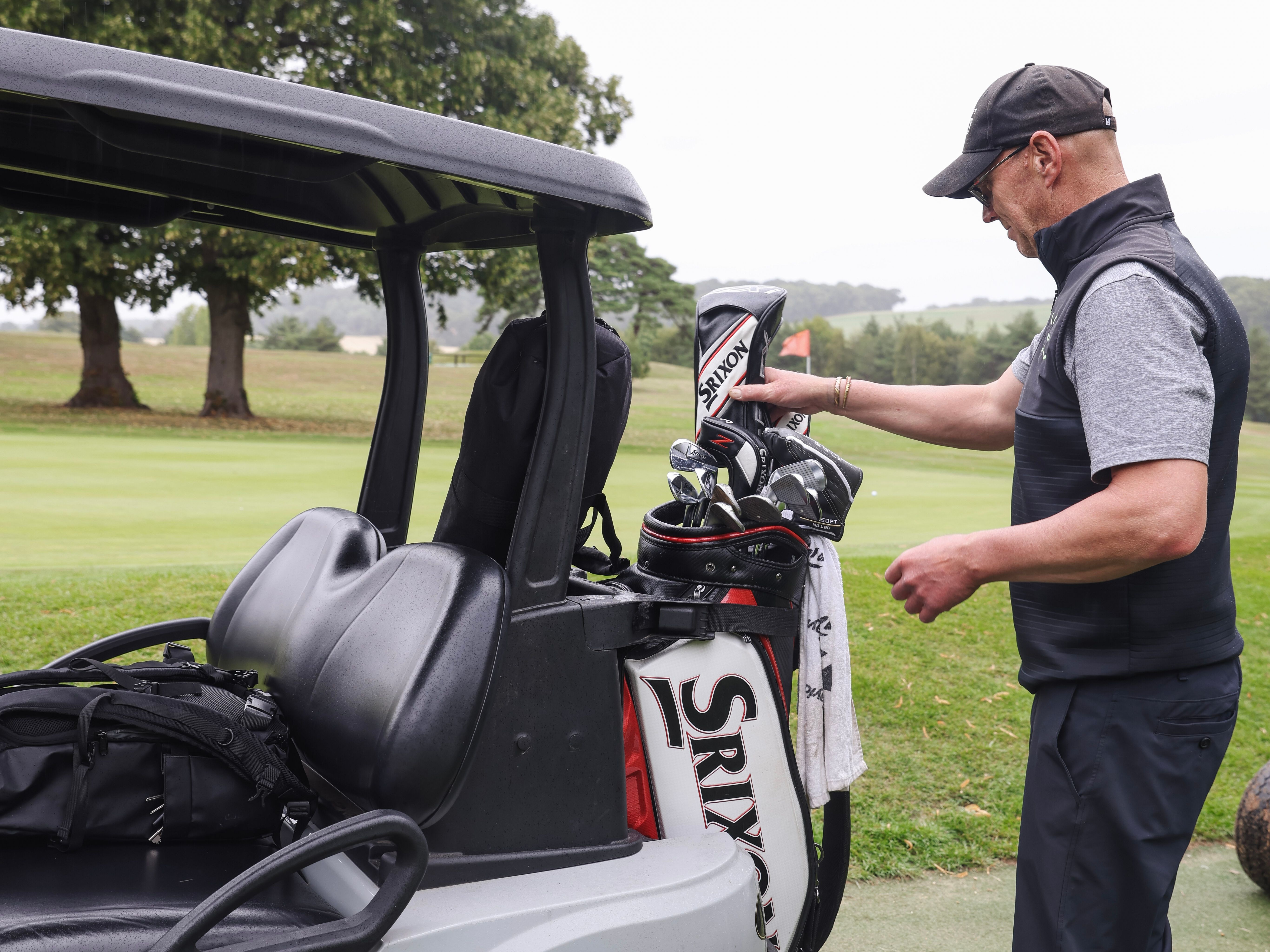Man preparing golf clubs beside a golf cart on a golf course